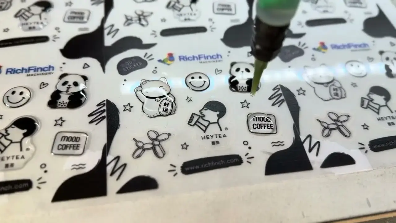 Dispensing needle laying resin onto a sheet of stickers on the Finch500, the opening frame of the video