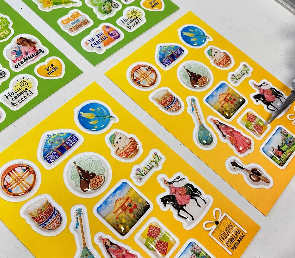 Yellow and green sheets of domed stickers with hand-drawn illustrations, seen from above at an angle