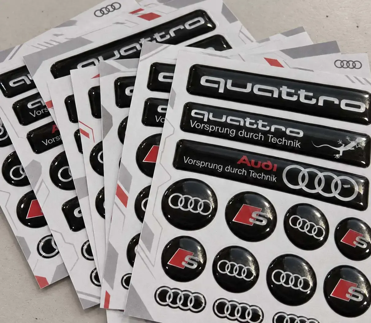 Fanned sheets of domed car-brand decals: lettering strips and round logo stickers