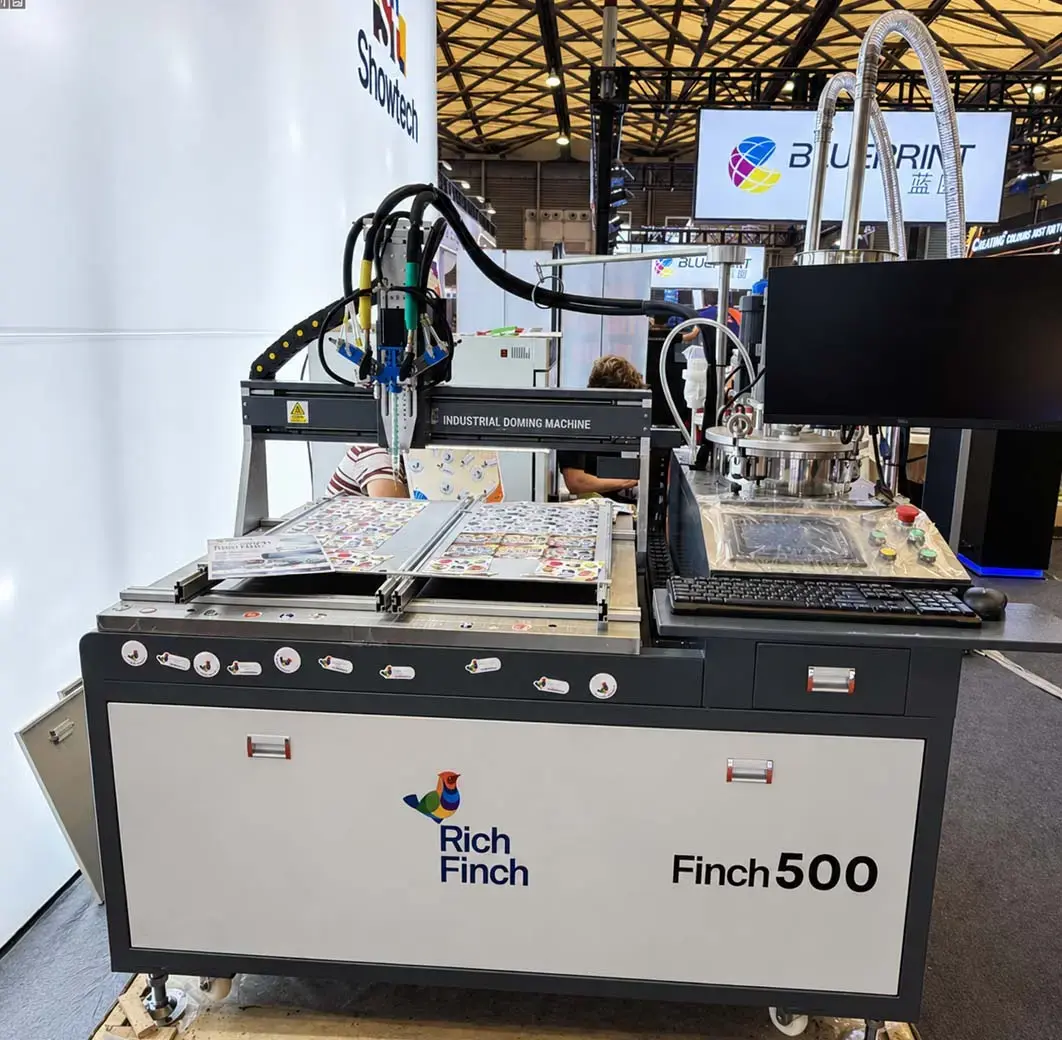 Finch500 doming machine on a trade-show stand, a sheet of stickers on its work table