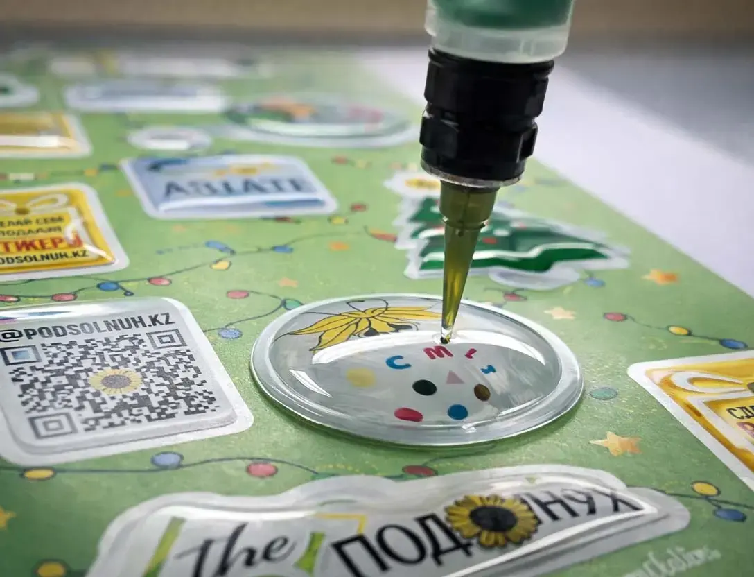 Dispensing needle laying clear resin onto a round sticker, finished domes on the sheet around it